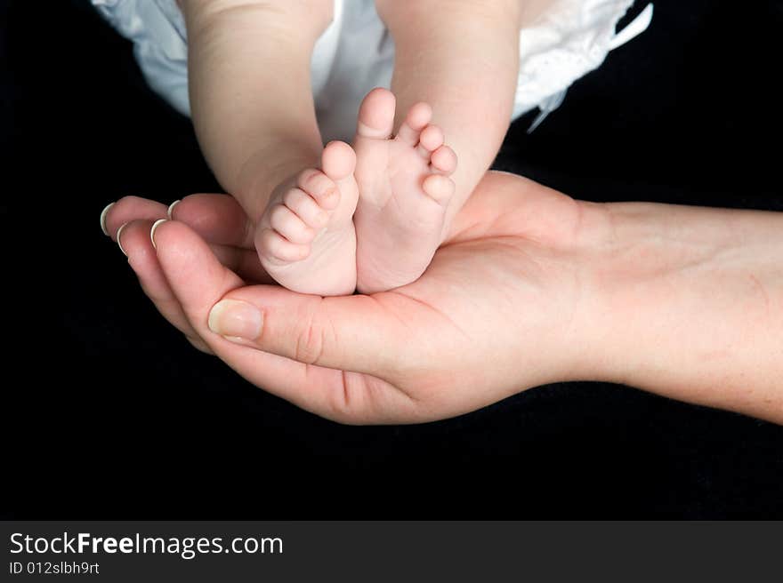 New born baby's feet supported in parent's hand shown on a black background. New born baby's feet supported in parent's hand shown on a black background.