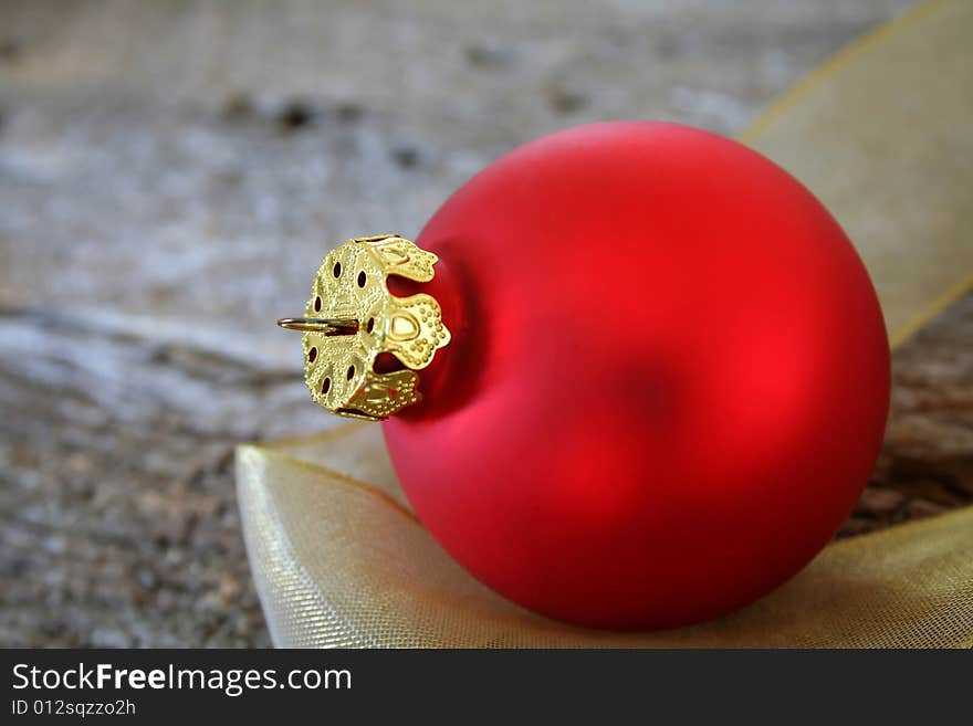 A single red Christmas ornament on a piece of gold ribbon and a wood textured background for the feel of a country Christmas.