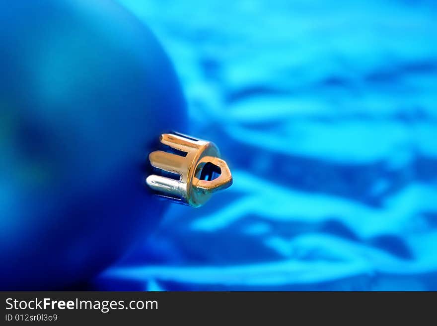 Close up of a blue Christmas ornament with a blue background.  Focus is on the cap of the ornament.  Copy space available.