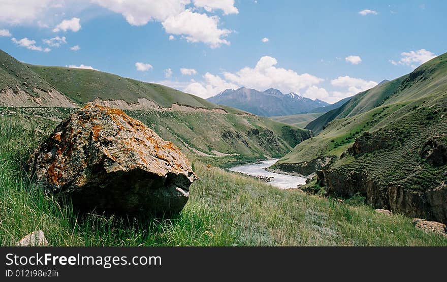 The big stone and the mountain river on a background of mountains and the blue sky. The big stone and the mountain river on a background of mountains and the blue sky