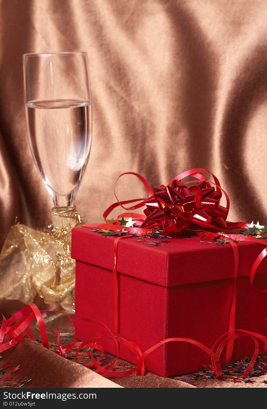 Party theme - red gift box with bows and stars with a glass of champagne on golden silk background