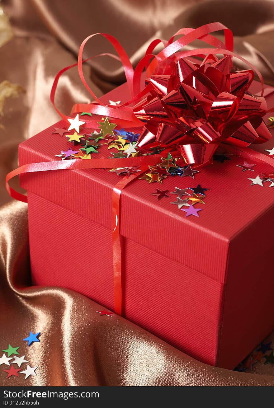 Red gift box with bows and stars on golden silk background