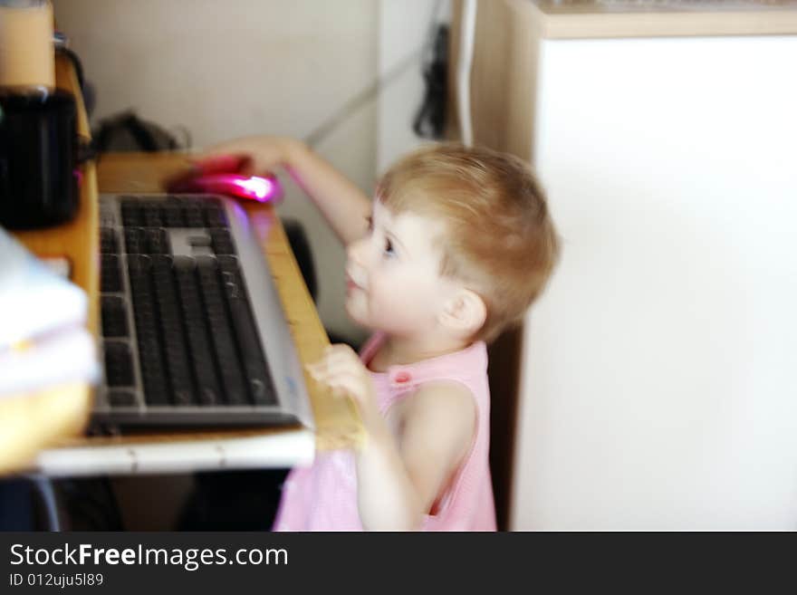 Little girl with hand on the computer's mouse looking at the display in motion blur. Little girl with hand on the computer's mouse looking at the display in motion blur