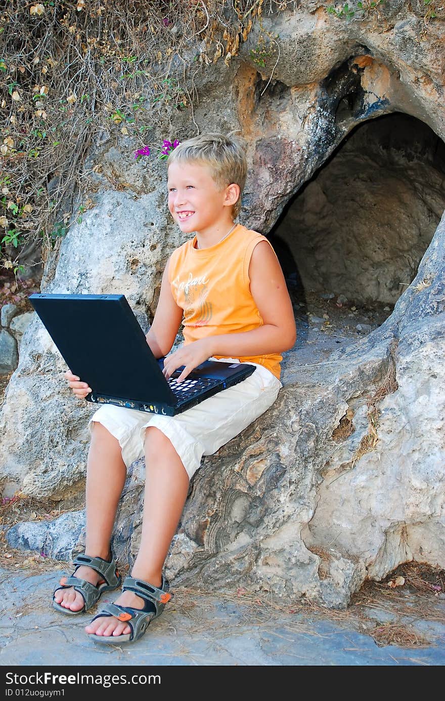 Cheerful boy plays on laptop near a cave