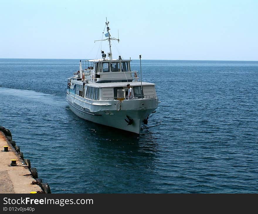 Small passenger cutter is about docking to concrete pier. This vessel is used to transport tourists by sea. Small passenger cutter is about docking to concrete pier. This vessel is used to transport tourists by sea.