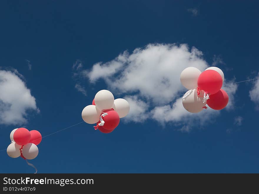 Red and white balloons with ribbons against blue sky.