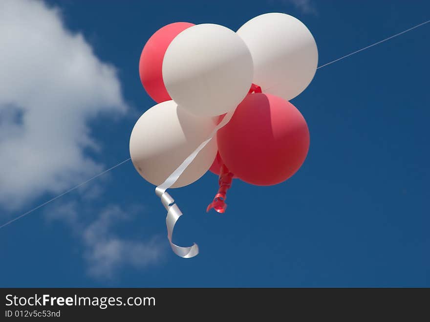 Red and white balloons with ribbons against blue sky.