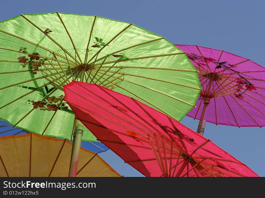 Colorful Asian-style paper parasols against a clear blue sky. Focus on center working of green parasol. Colorful Asian-style paper parasols against a clear blue sky. Focus on center working of green parasol.