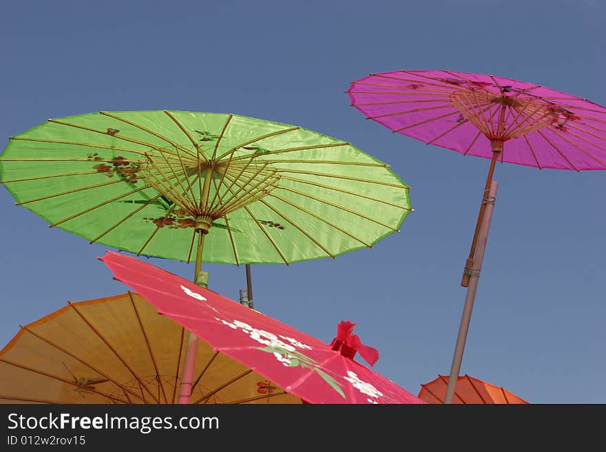 Colorful Asian-style paper parasols against a clear blue sky. Focus on center working of green parasol. Colorful Asian-style paper parasols against a clear blue sky. Focus on center working of green parasol.