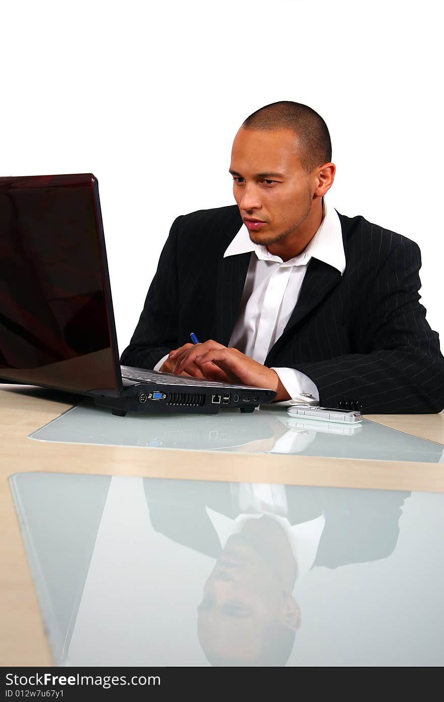 A young businessman sitting by desk at office working on the laptop with cellphone on the table. A young businessman sitting by desk at office working on the laptop with cellphone on the table.