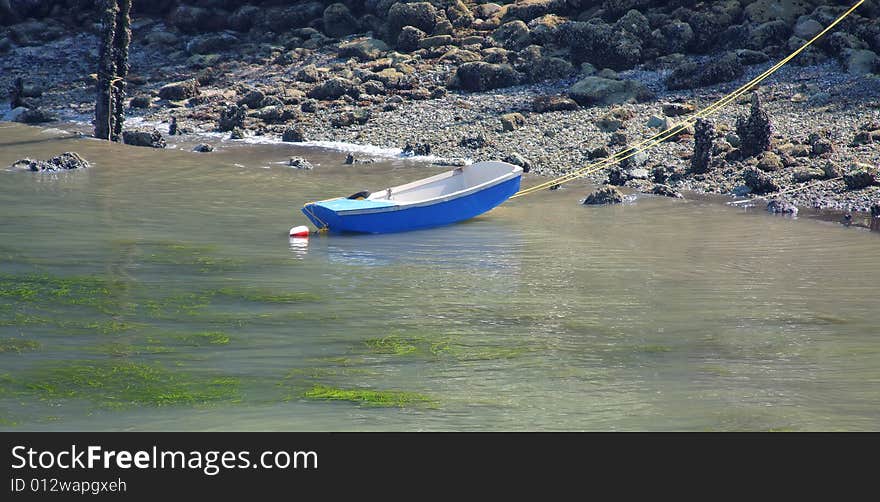 Rowboat anchored near the beach at low tide with a yellow rope running to shore. Rowboat anchored near the beach at low tide with a yellow rope running to shore.