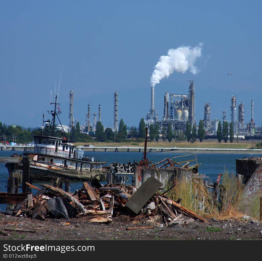 View of an oil refinery from a junked dock area, with trash and vandalism in the foreground. View of an oil refinery from a junked dock area, with trash and vandalism in the foreground.