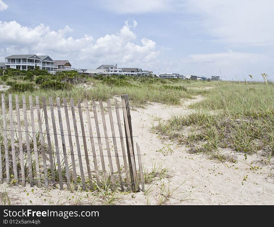 Wooden beach fence segregates the shore line beach from the large vacation homes. Wooden beach fence segregates the shore line beach from the large vacation homes.