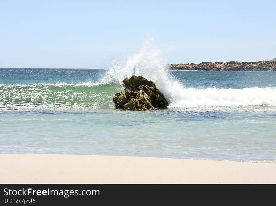 A wave crashing over a large rock in the summer time. A wave crashing over a large rock in the summer time