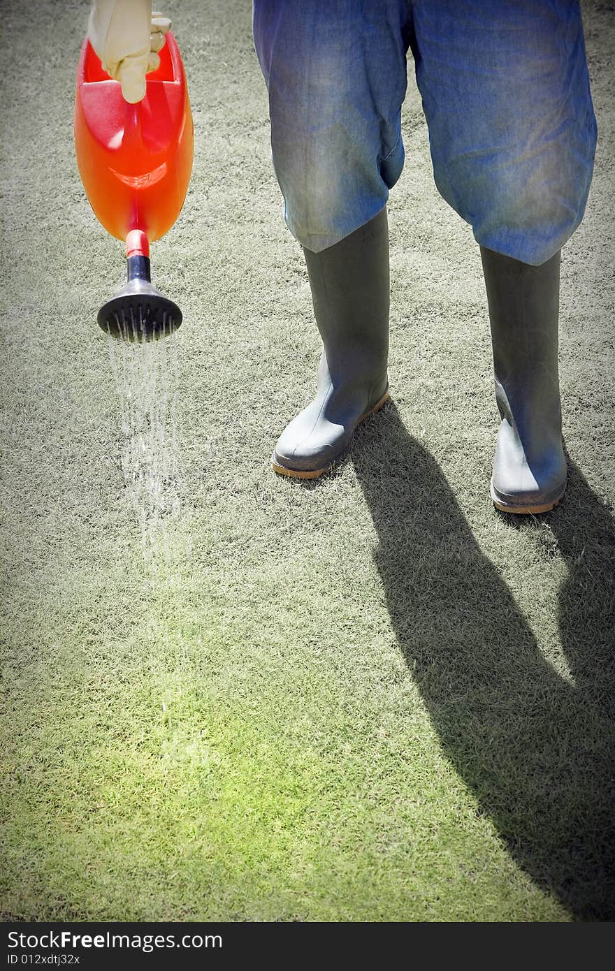 Cropped view of person in boots watering grass with watering can. Cropped view of person in boots watering grass with watering can