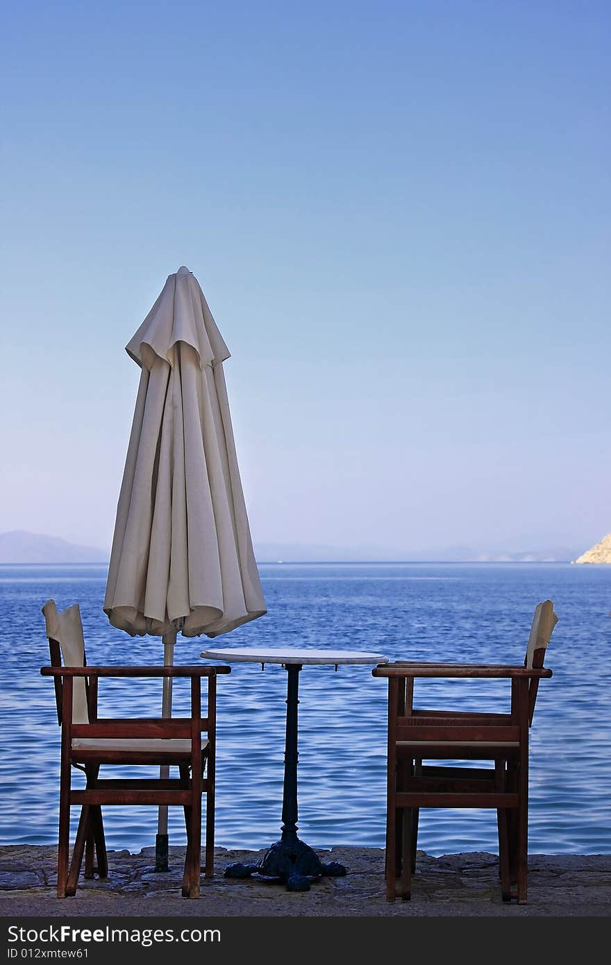 Two empty wooden chairs on the edge of the ocean (Greek islands). Two empty wooden chairs on the edge of the ocean (Greek islands).