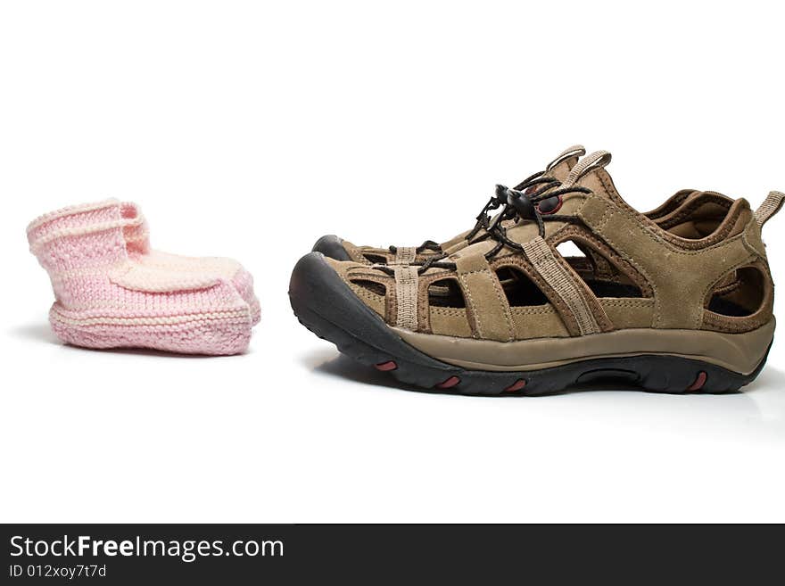 Pink baby bootees standing opposite large male shoes, isolated, on white background. Pink baby bootees standing opposite large male shoes, isolated, on white background