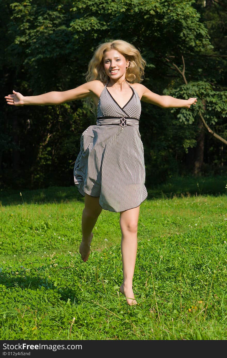 Girl in a summer dress runs on a green grass on a background of trees. Girl in a summer dress runs on a green grass on a background of trees