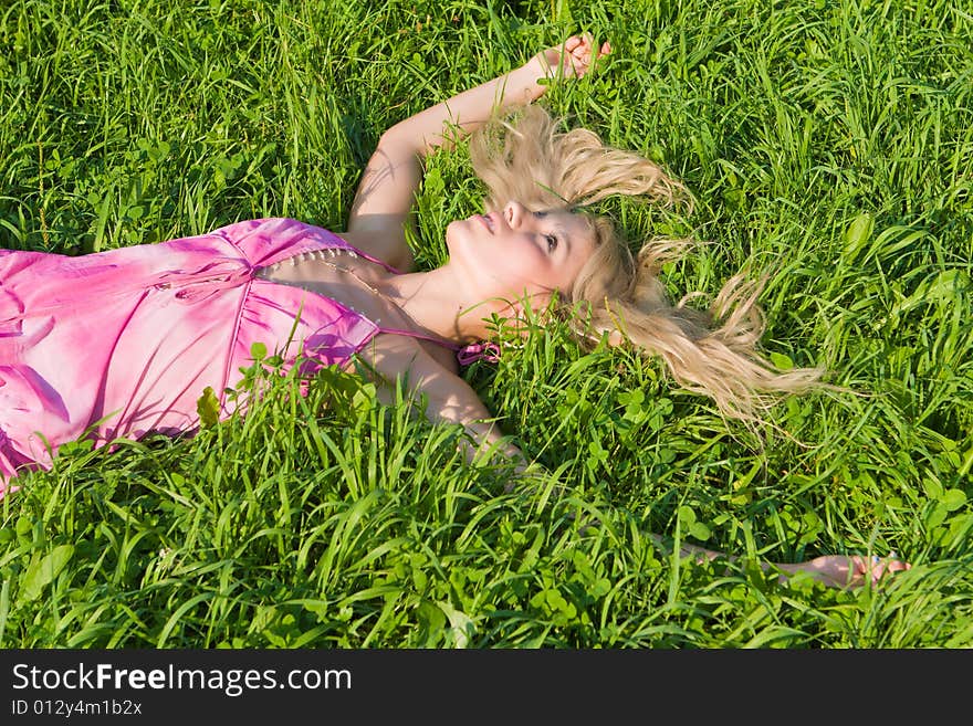 Girl in a pink summer dress has a rest on a green grass. Girl in a pink summer dress has a rest on a green grass