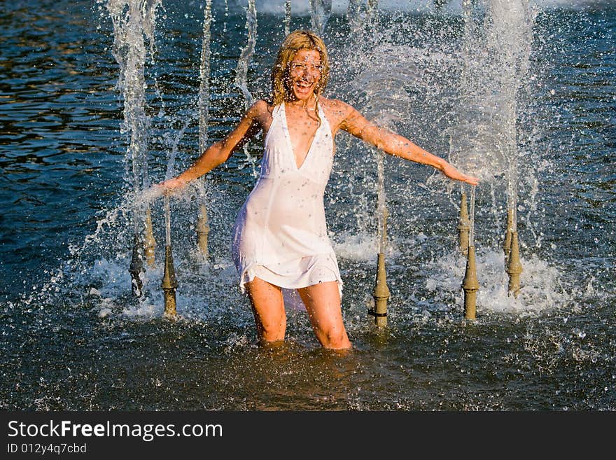 Beautiful girl in a white dress laps in jets of a fountain. Beautiful girl in a white dress laps in jets of a fountain