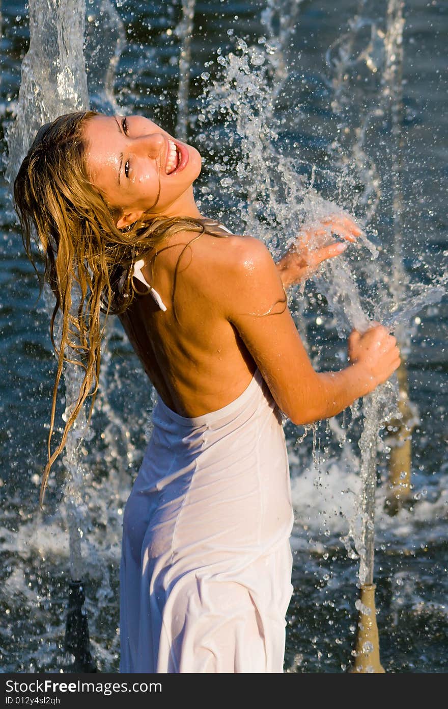 Beautiful girl in a white dress laps in jets of a fountain. Beautiful girl in a white dress laps in jets of a fountain