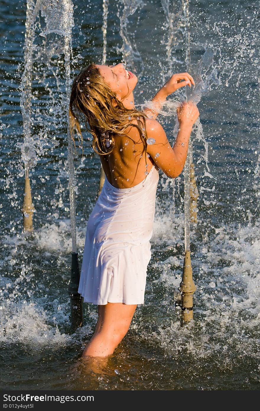 Beautiful girl in a white dress laps in jets of a fountain. Beautiful girl in a white dress laps in jets of a fountain