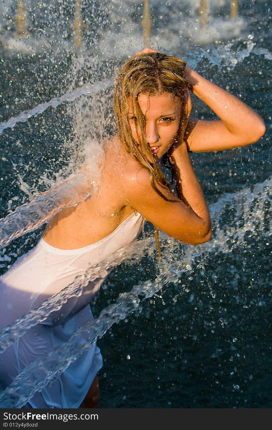 Beautiful girl in a white dress laps in jets of a fountain. Beautiful girl in a white dress laps in jets of a fountain