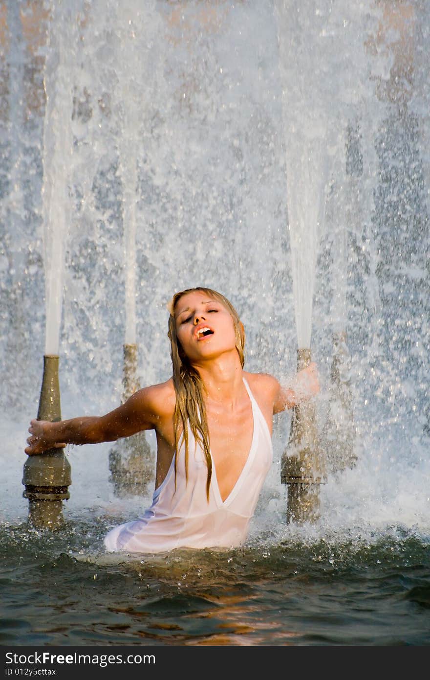 Beautiful girl in a white dress laps in jets of a fountain. Beautiful girl in a white dress laps in jets of a fountain