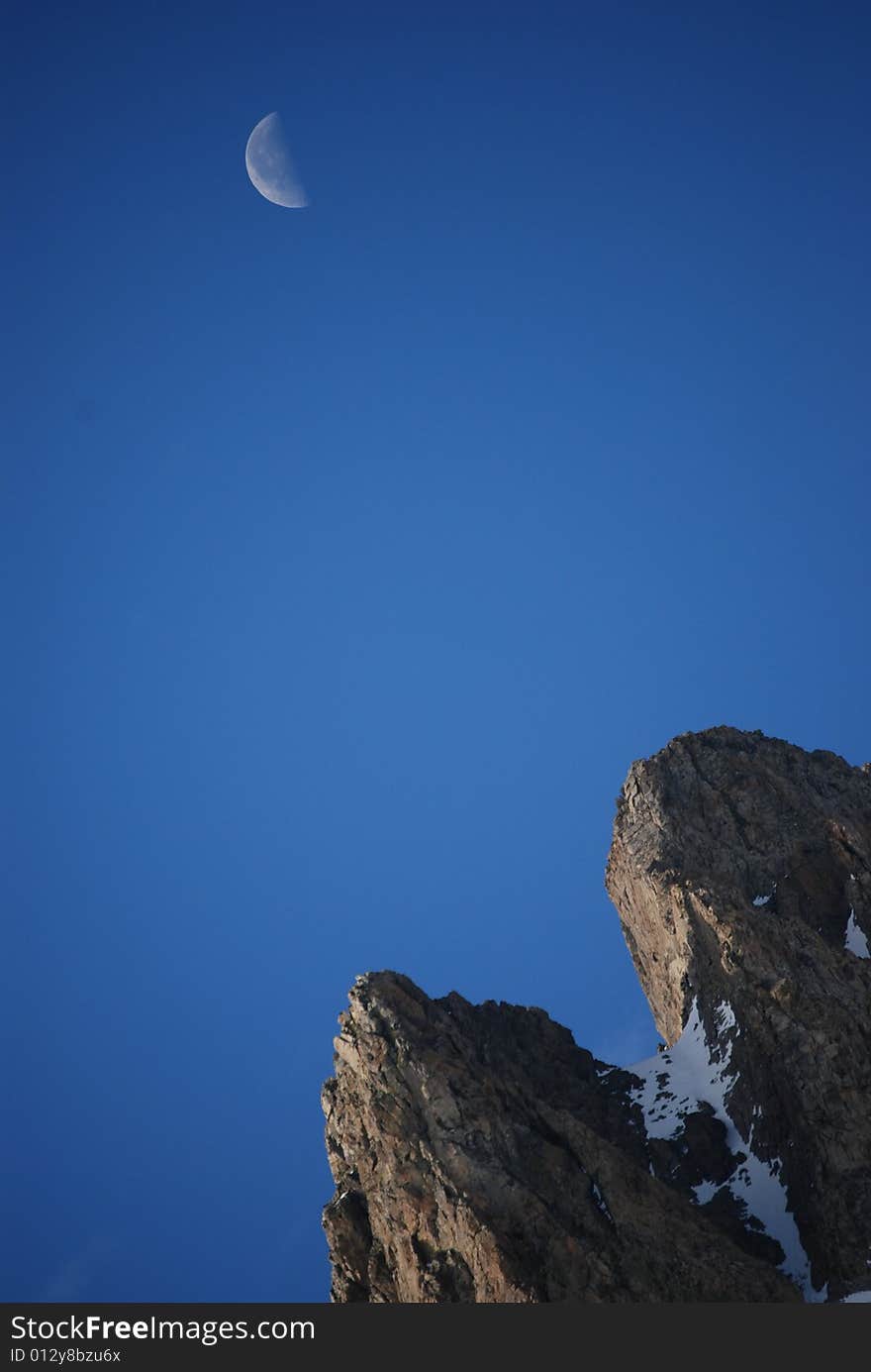 Sunrise over June Lake  peak, while the moon is still out, dark blue background. Sunrise over June Lake  peak, while the moon is still out, dark blue background