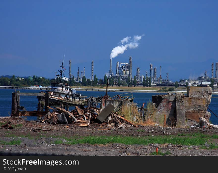 View of an oil refinery from a dock area across the bay, with trash and vandalism in the foreground.