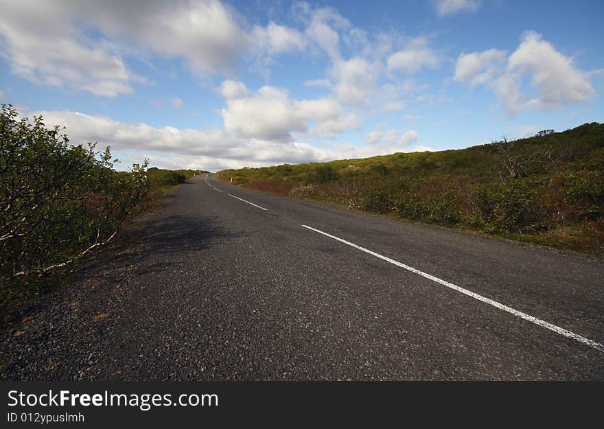 Sunlit road disappearing into the distance under the partially cloudy sky.