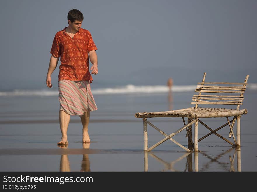 Man is walking on the the beach near a trestle-bed. Man is walking on the the beach near a trestle-bed