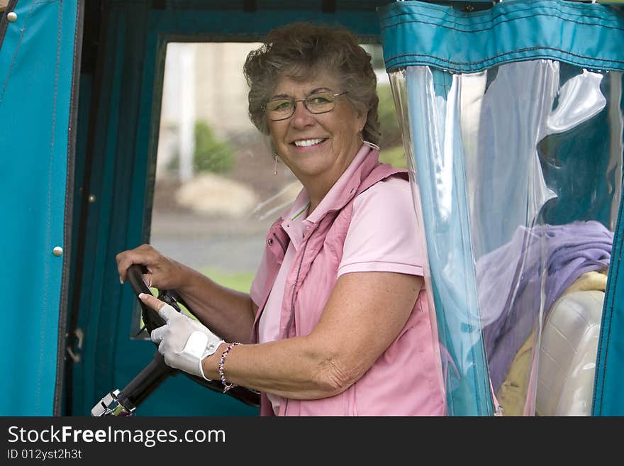 Elderly woman with golf glove smiling as she rides in a golf cart. Vertically framed photo. Elderly woman with golf glove smiling as she rides in a golf cart. Vertically framed photo.