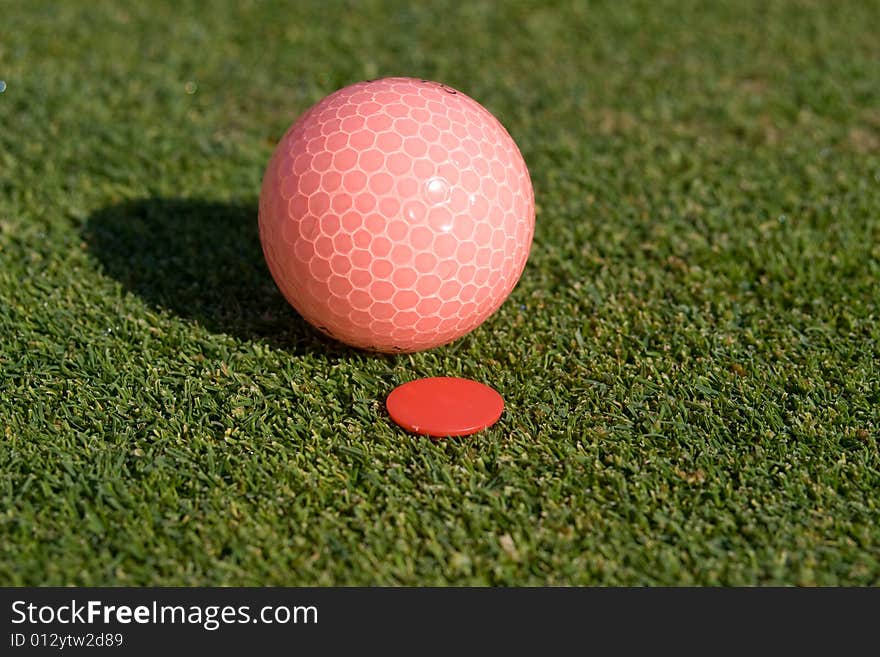 Pink golfball rests on green next to golfball marker. Horizontally framed photo. Pink golfball rests on green next to golfball marker. Horizontally framed photo.