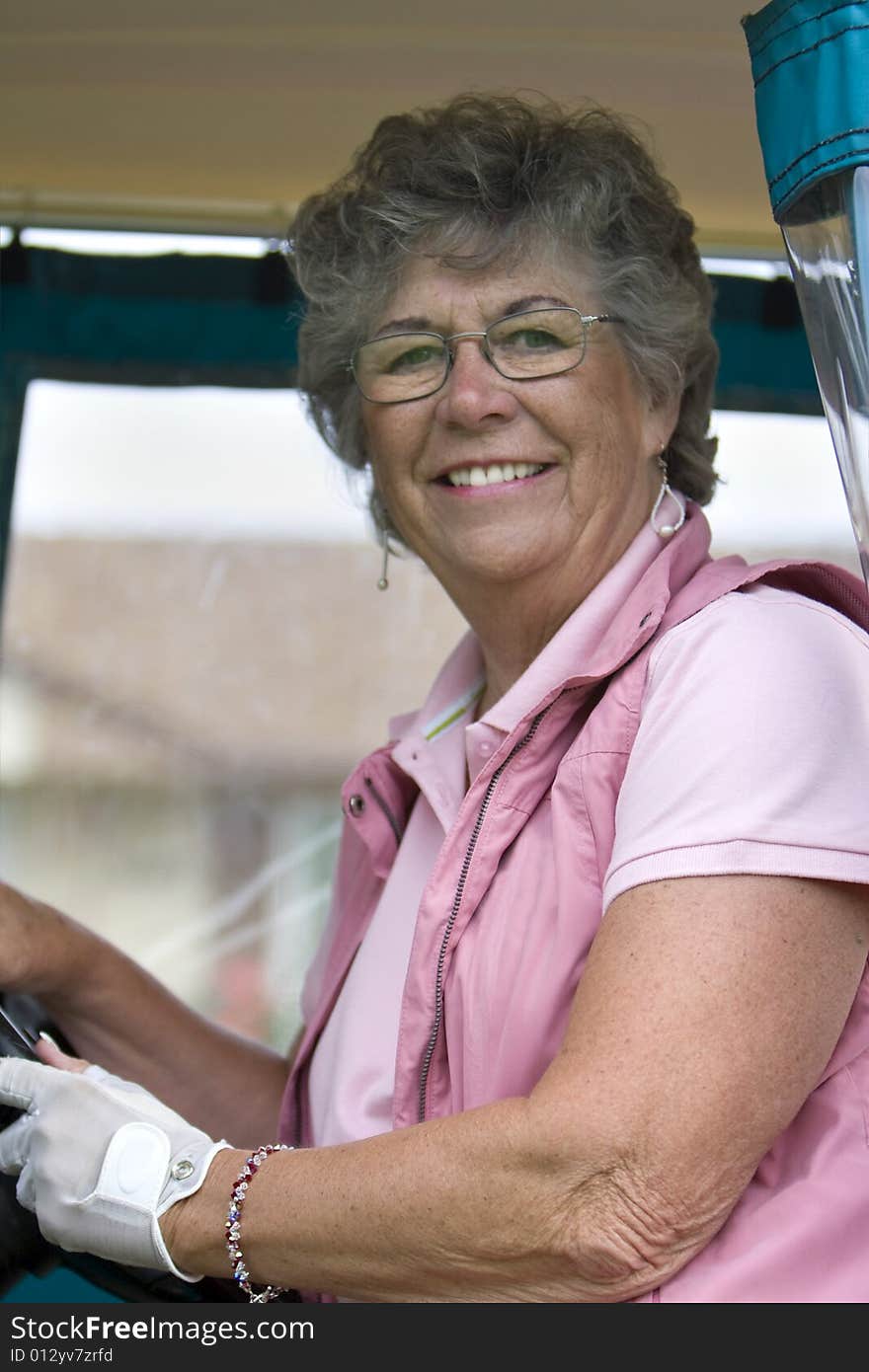 Elderly woman with golf glove smiling as she rides in a golf cart. Vertically framed photo. Elderly woman with golf glove smiling as she rides in a golf cart. Vertically framed photo.