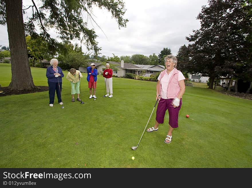 Five elderly women playing golf and laughing. Horizontally framed photo.