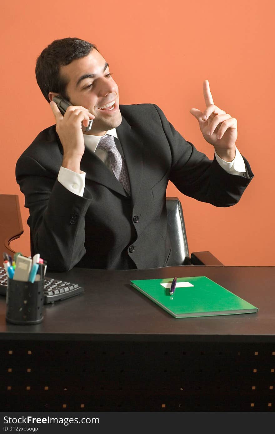 Businessman sits at his desk and speaks animatedly on his phone. Vertically framed photograph. Businessman sits at his desk and speaks animatedly on his phone. Vertically framed photograph.