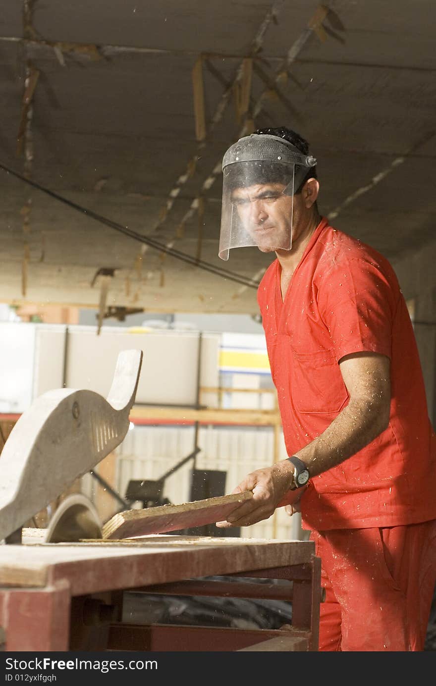 Construction worker rips board with table saw. He is wearing an orange suit and a face mask. Vertically framed photo. Construction worker rips board with table saw. He is wearing an orange suit and a face mask. Vertically framed photo.