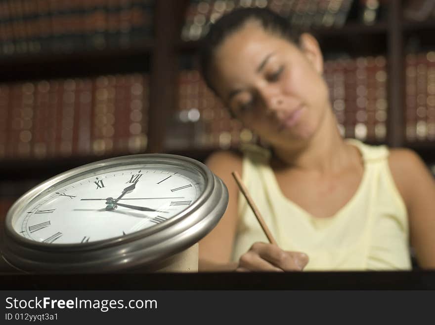 Woman working at desk with a clock in the foreground. Horizontally framed photo. Woman working at desk with a clock in the foreground. Horizontally framed photo.