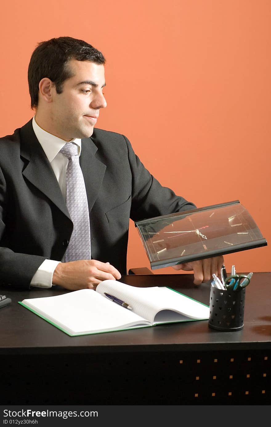 Business man smiles as he sits at his desk looking at his clock. Vertically framed photo. Business man smiles as he sits at his desk looking at his clock. Vertically framed photo.