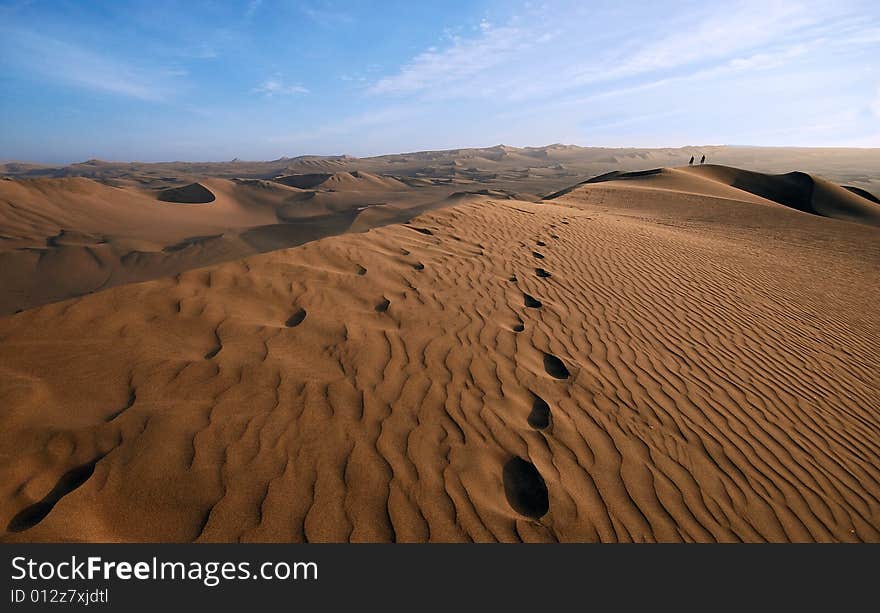 Men walking in the midlle of a huge sand dune