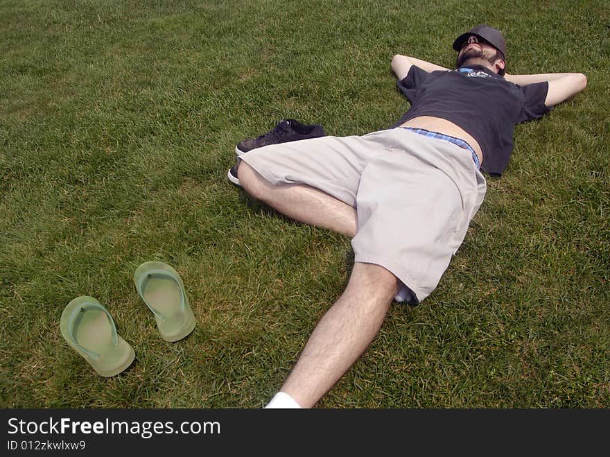 A man with a hat over his head resting in the grass. A man with a hat over his head resting in the grass.