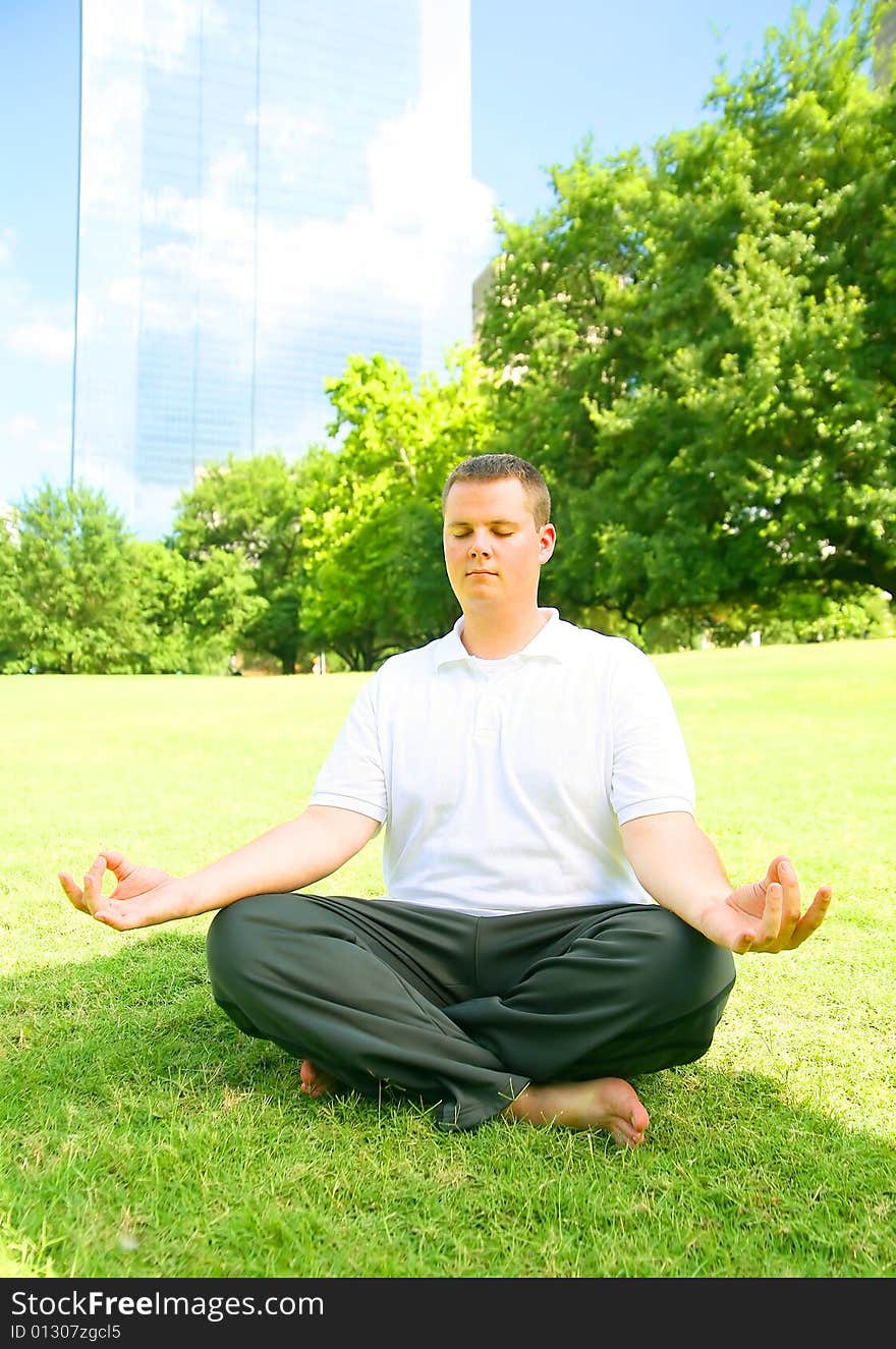 Handsome caucasian man meditate outdoor in a park with downtown building in the background. concept for yoga or wellbeing. Handsome caucasian man meditate outdoor in a park with downtown building in the background. concept for yoga or wellbeing