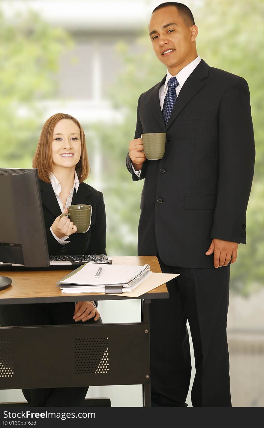 Two business people, one standing and the other sitting. both look at camera and smile. concept for business team, office break or team work. Two business people, one standing and the other sitting. both look at camera and smile. concept for business team, office break or team work