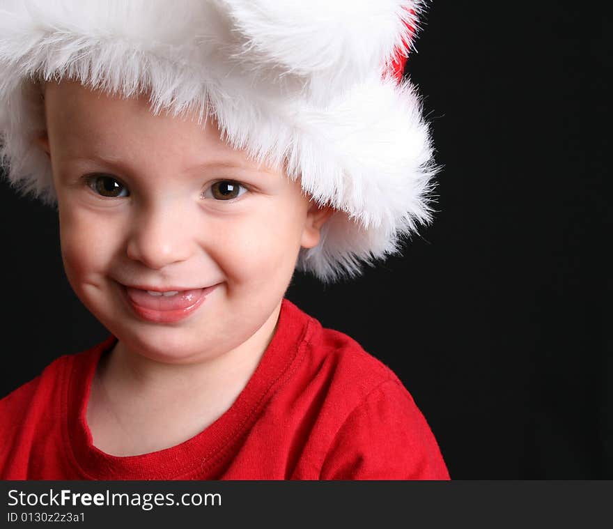 Blonde toddler against a black background wearing a christmas hat