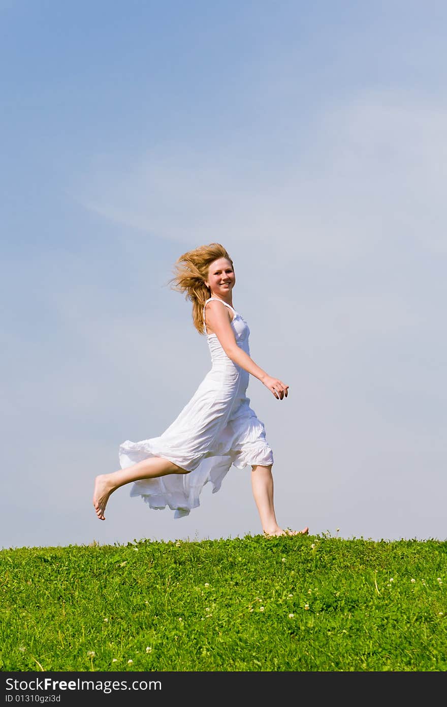 Girl runs on a grass on a background of the blue sky