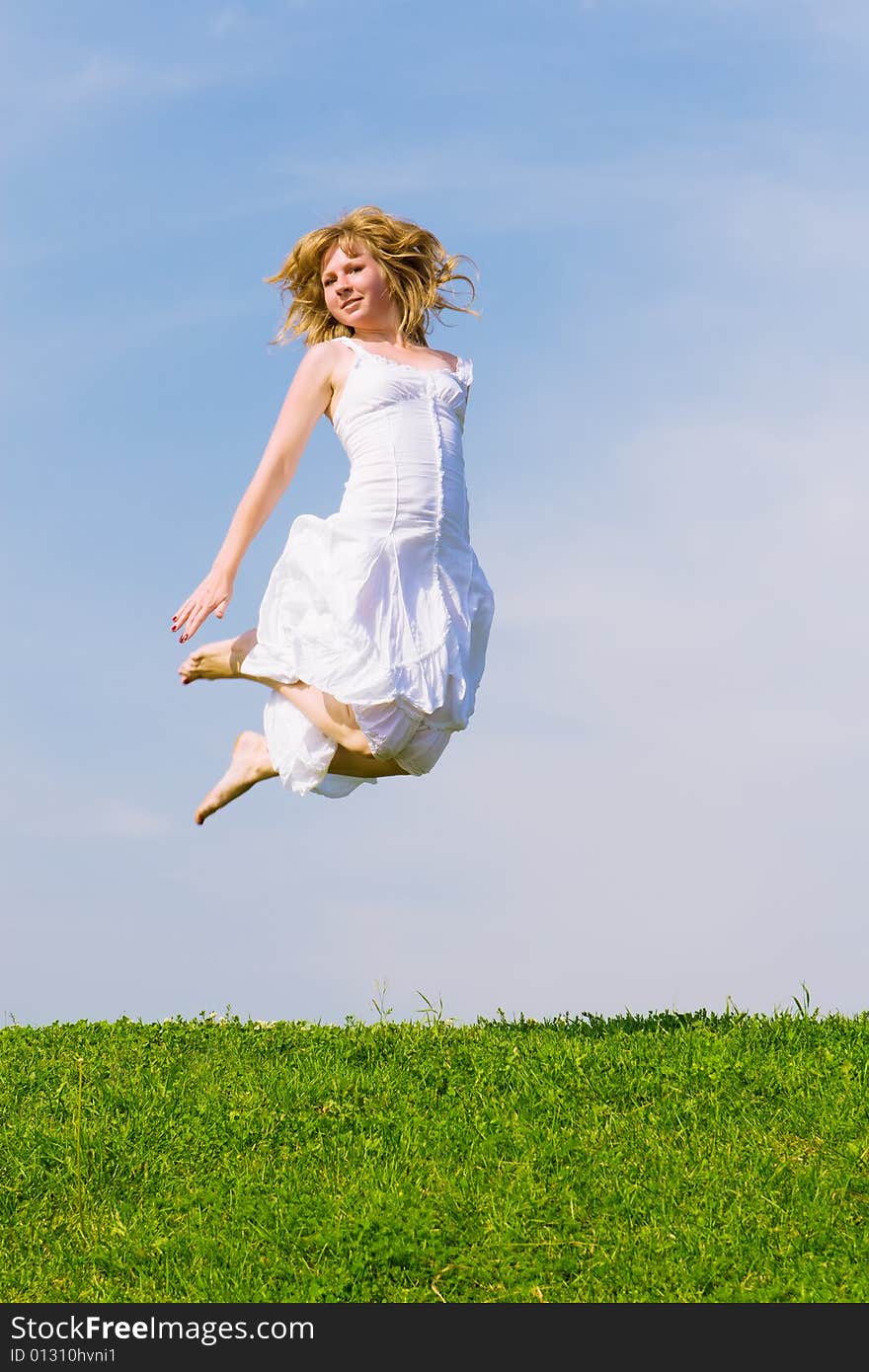 Girl jumps on a green grass on a background of the blue sky. Girl jumps on a green grass on a background of the blue sky