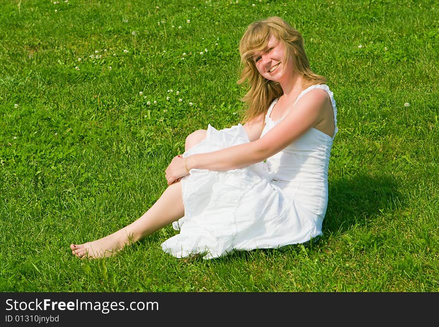 Girl in a white dress sits on a green grass. Girl in a white dress sits on a green grass