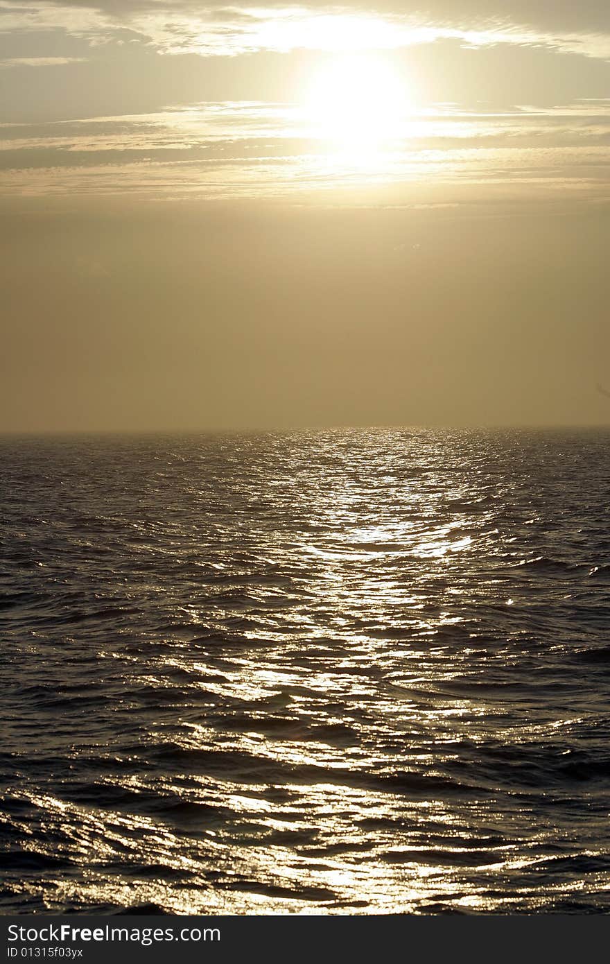 The ocean at dusk, the sun peaking through the clouds