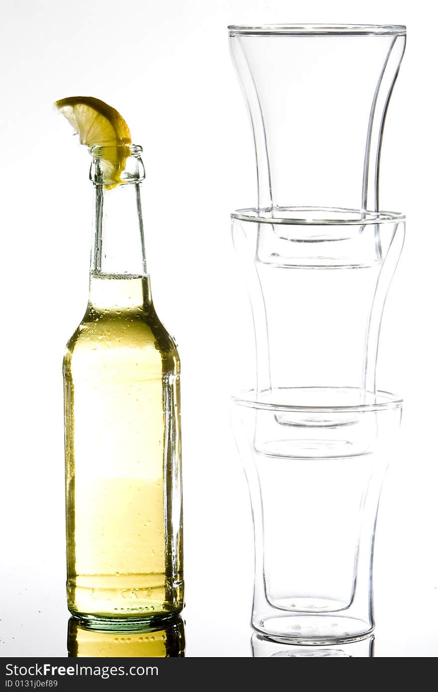 A bottle of beer standing next to a pile of three glasses. A bottle of beer standing next to a pile of three glasses.